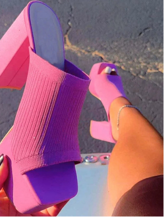 Purple and pink high-heeled shoes held by a person against a blurred background