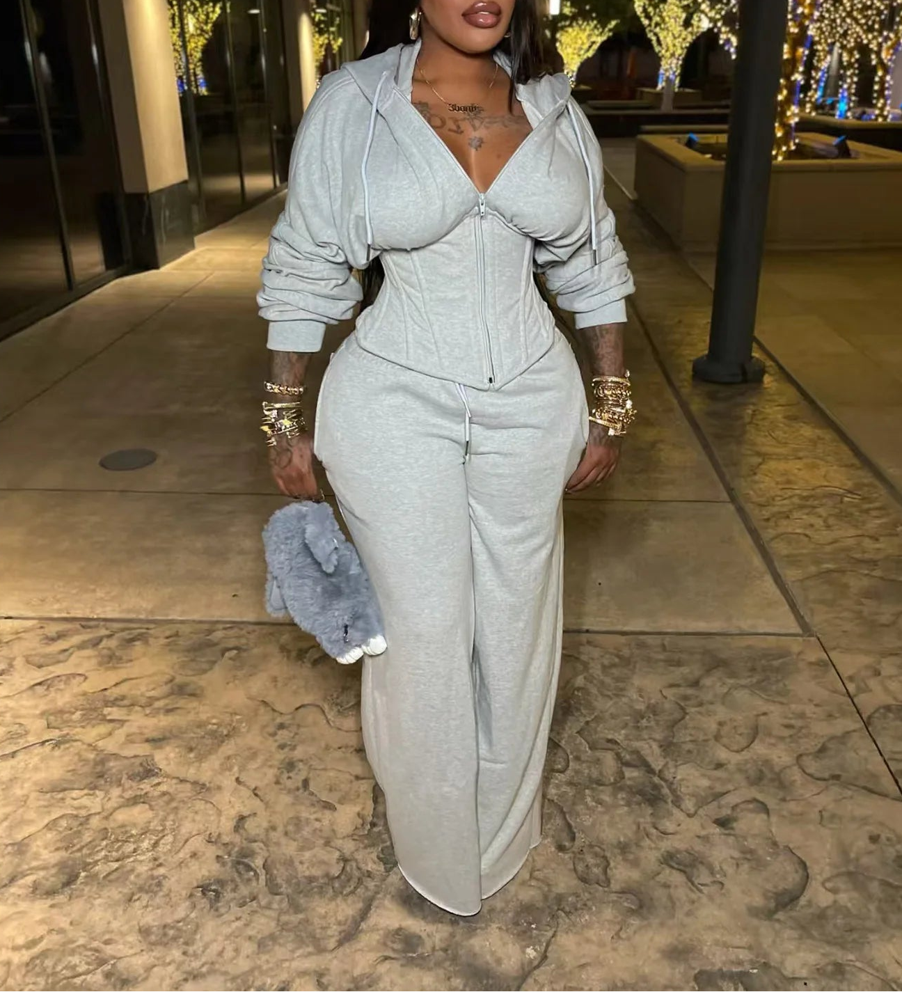 Woman in a gray outfit standing on a sidewalk at night.