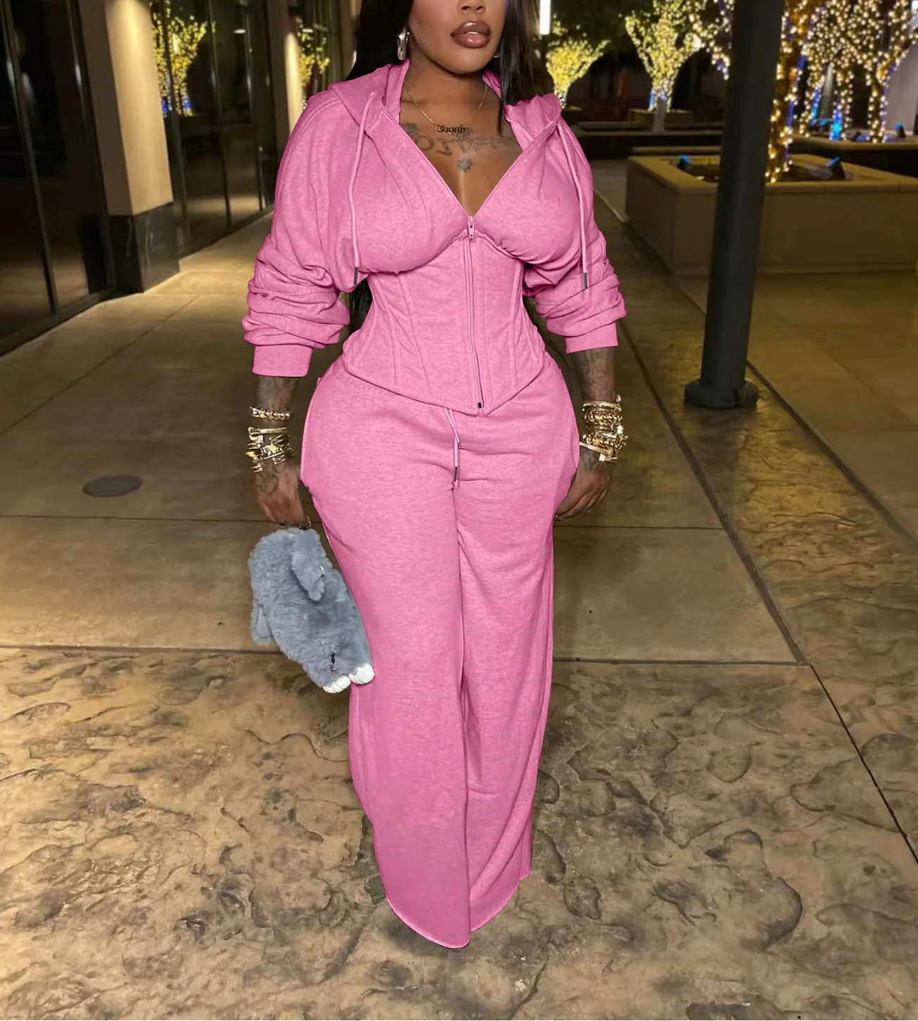 Woman in a pink outfit standing on a sidewalk at night.