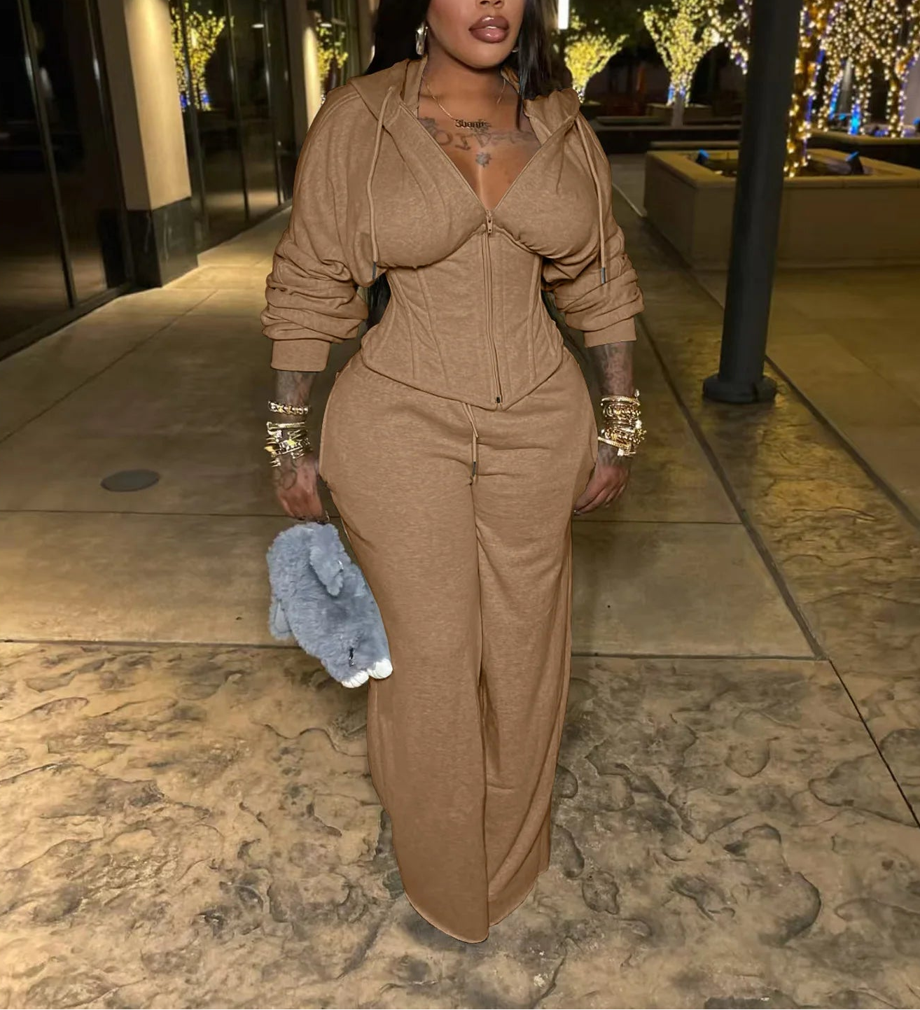 Woman in a beige outfit standing on a sidewalk at night.