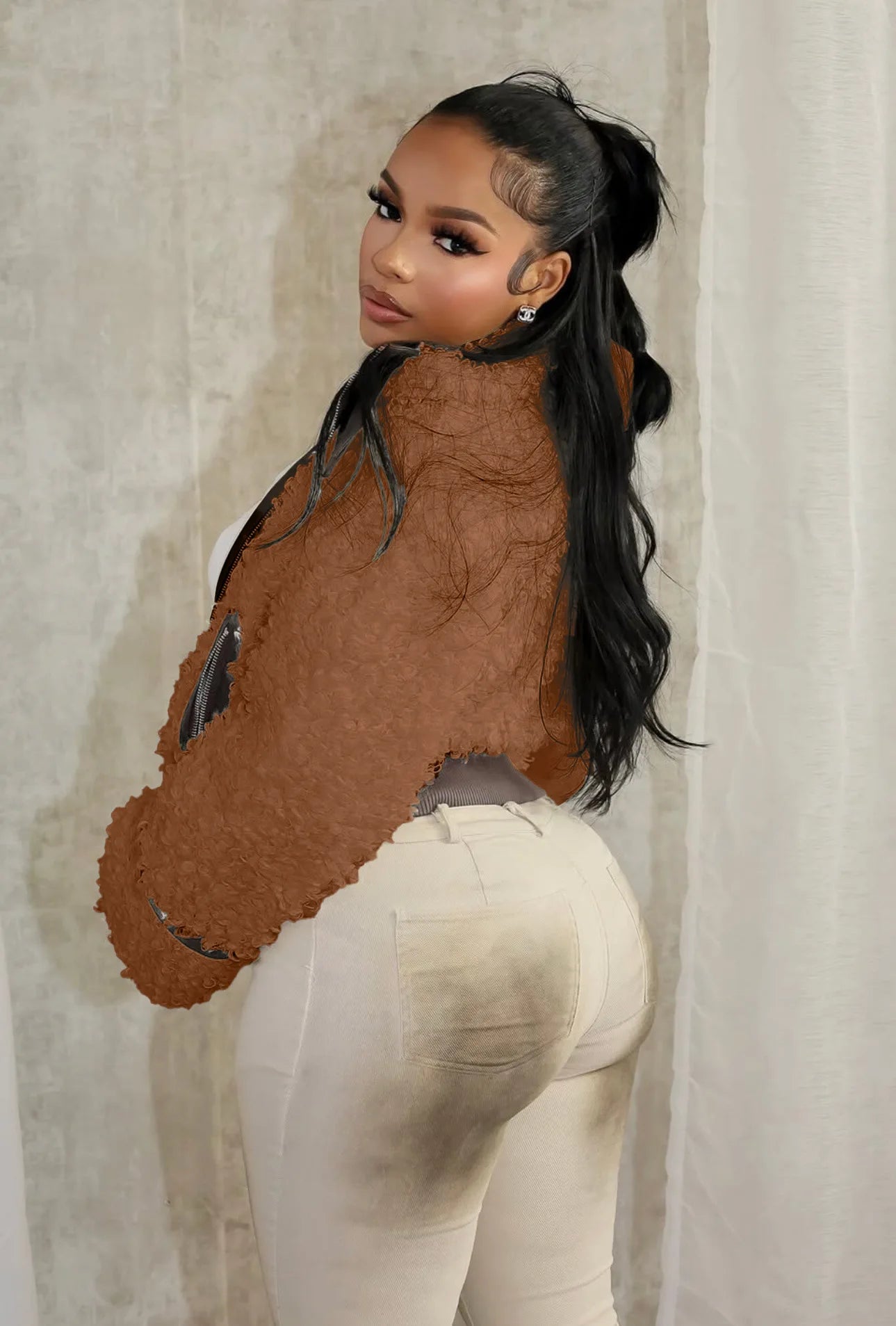 Person wearing a brown textured top and white pants against a neutral background